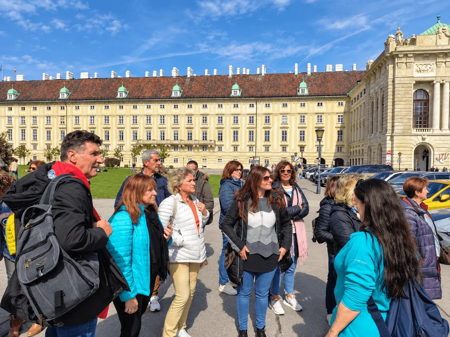 Un groupe de touristes écoutant son guide sur la Heldenplatz à Vienne, avec la longue aile jaune du palais de la Hofburg derrière eux.