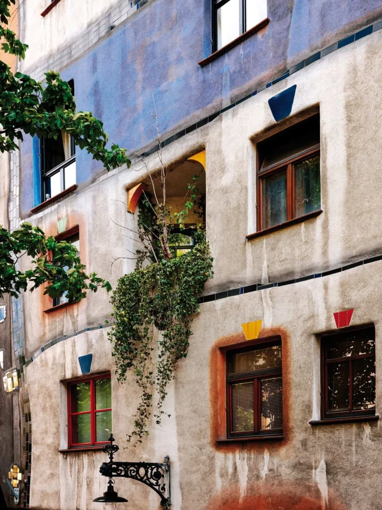 The irregular painted facade of the Hundertwasserhaus in Vienna, with coloured window frames and ivy trailing from a balcony.