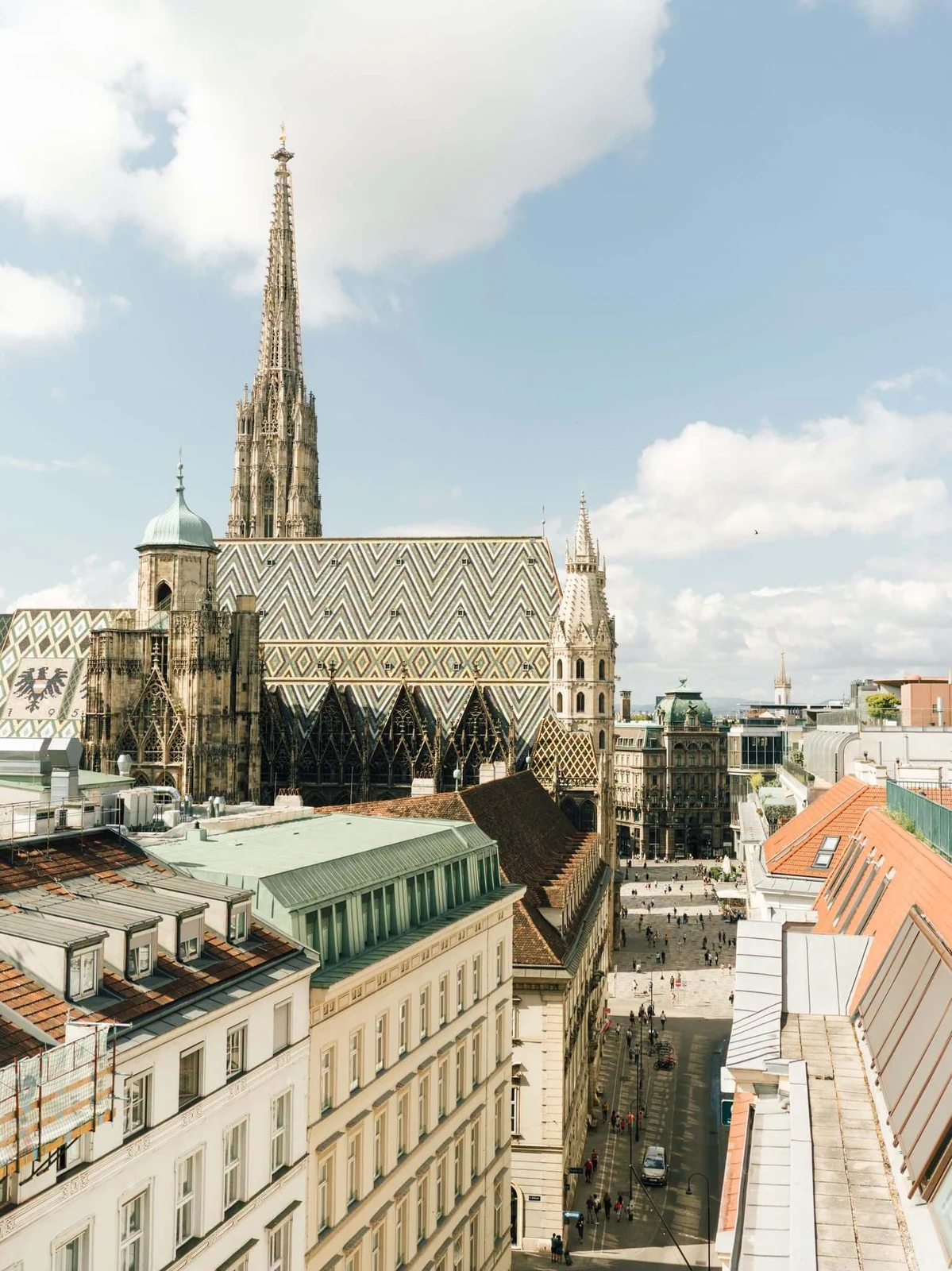St Stephen's Cathedral in Vienna from the rooftops, its Gothic spire and patterned tiled roof above the pedestrian Graben.