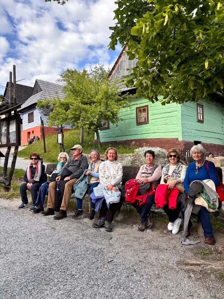 Visitors resting on a bench in front of the painted log houses of Vlkolínec, the UNESCO-listed village near Ružomberok.