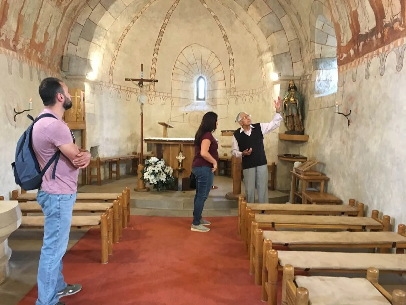 A guide showing visitors the medieval frescoes inside the Church of St Stephen the King in Žilina, with the barrel-vaulted nave and wooden benches around them.