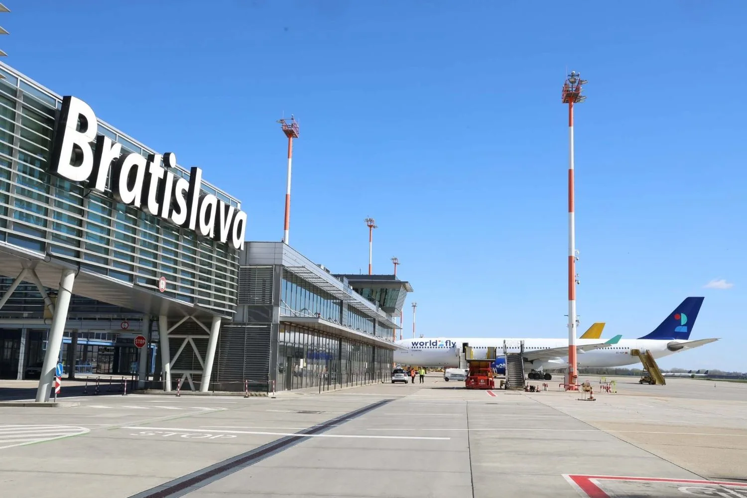 Das Hauptterminal des Flughafens M. R. Štefánik in Bratislava vom Vorfeld aus gesehen, mit dem Schriftzug Bratislava auf der Dachkante und einem Flugzeug dahinter.