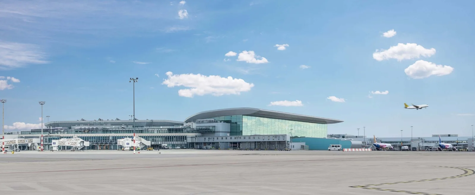 Terminal 2 at Budapest Ferenc Liszt International Airport seen across the apron, with aircraft at the gates and one climbing away overhead.