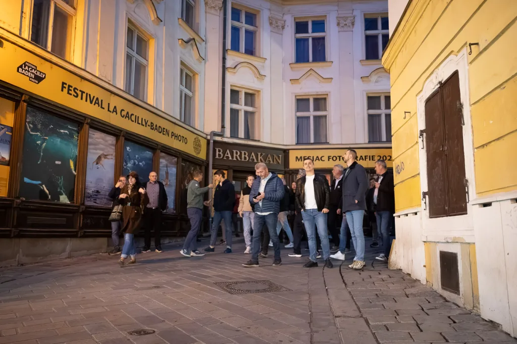 A corporate group gathered outside the Barbakan beside St Michael’s Gate in Bratislava, in front of the La Gacilly–Baden photo festival display windows.