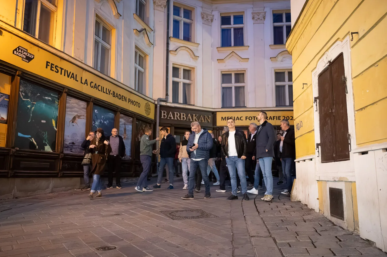 A corporate group gathered outside the Barbakan beside St Michael’s Gate in Bratislava, in front of the La Gacilly–Baden photo festival display windows.