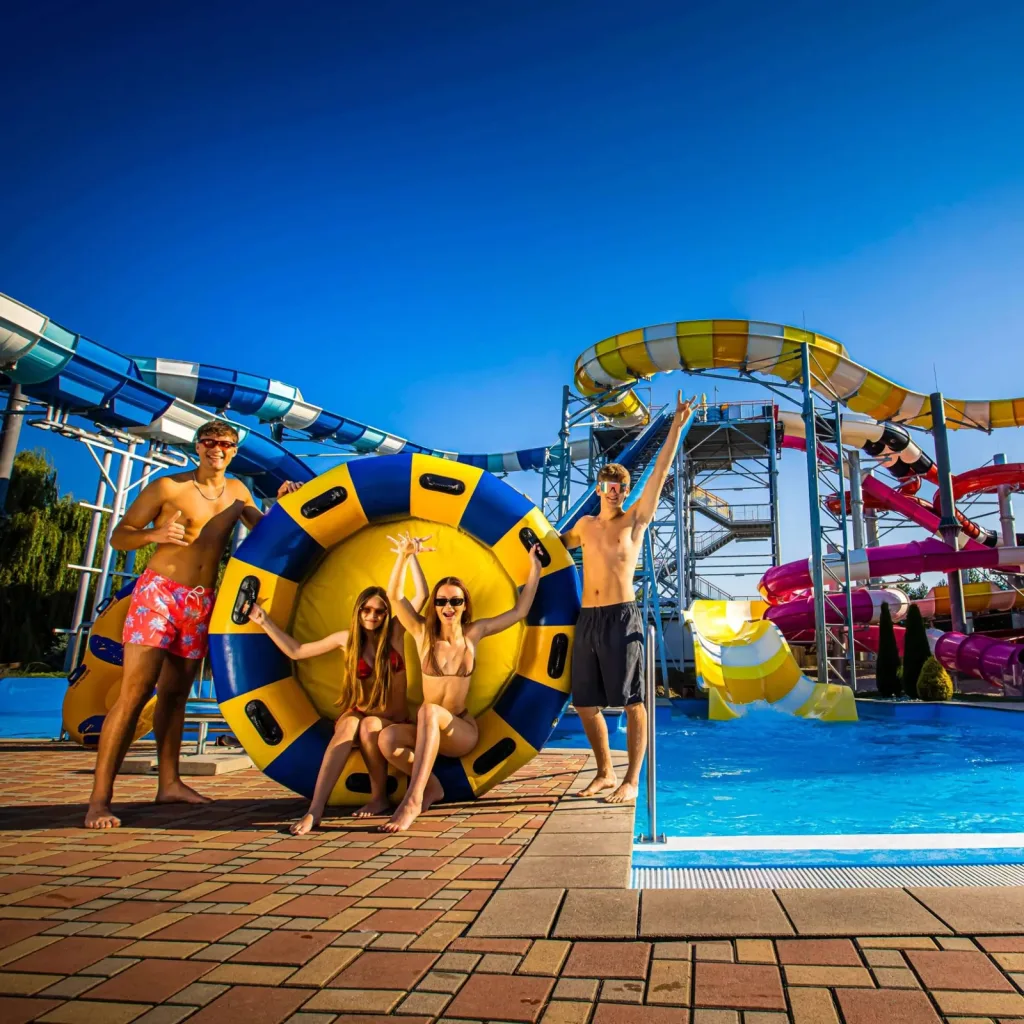 A family posing with a large rubber ring at a Slovak aquapark, water slides curving behind them under a deep blue sky.
