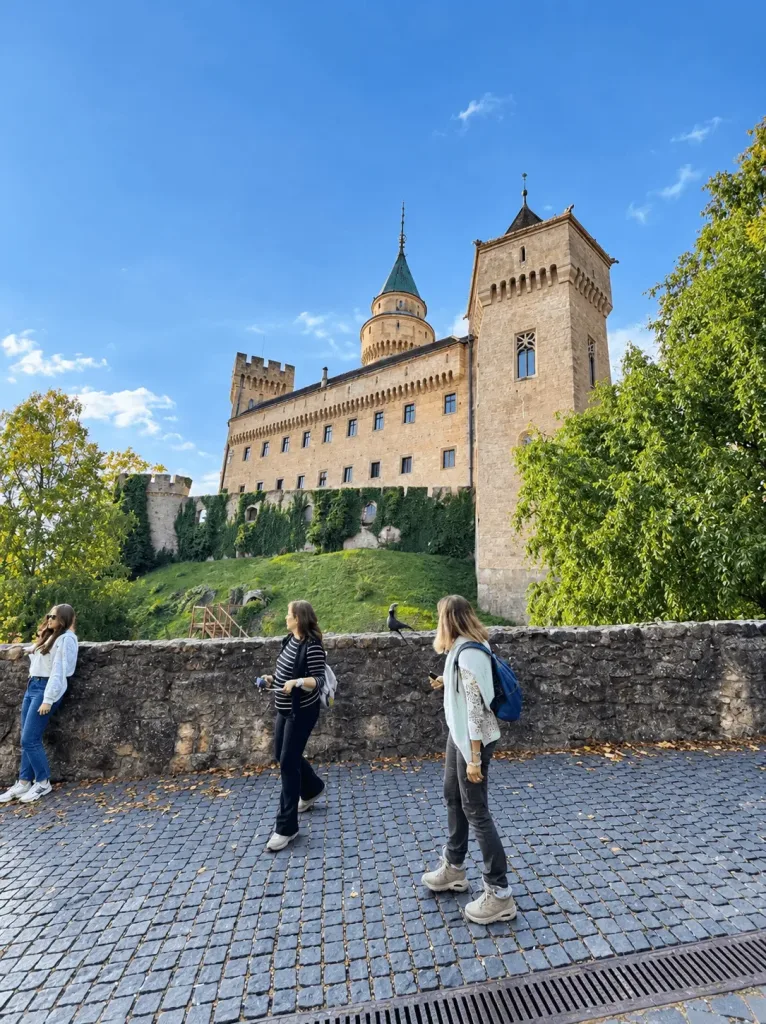 Visitors on the path below Bojnice Castle, its ochre walls, battlements and green-roofed tower rising above the ivy-covered rampart.