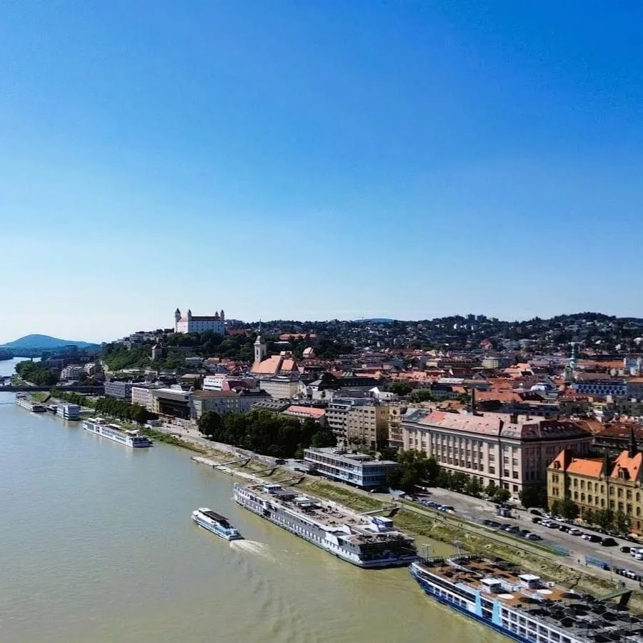 Bratislava from the air along the Danube, river cruise ships moored at the embankment and the castle on its hill above the old town.