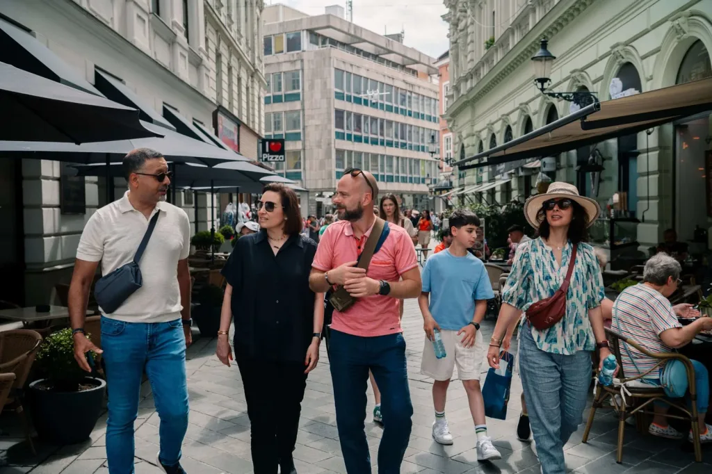 A family walking a pedestrian street in Bratislava’s old town, café terraces and parasols along both sides.