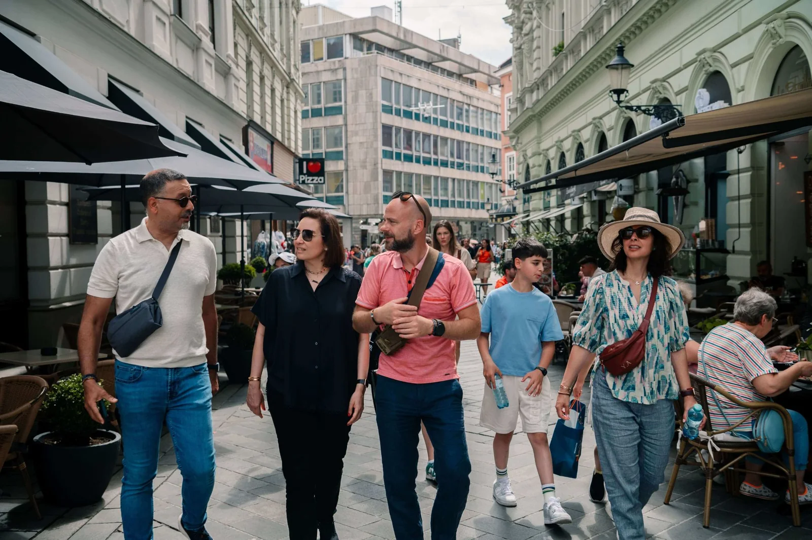 A family walking a pedestrian street in Bratislava’s old town, café terraces and parasols along both sides.