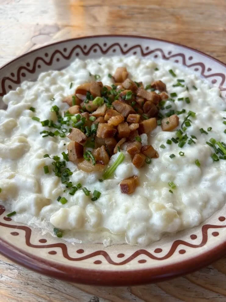 Bryndzové halušky — potato dumplings with sheep’s cheese, fried bacon and chives — served on a folk-painted plate.