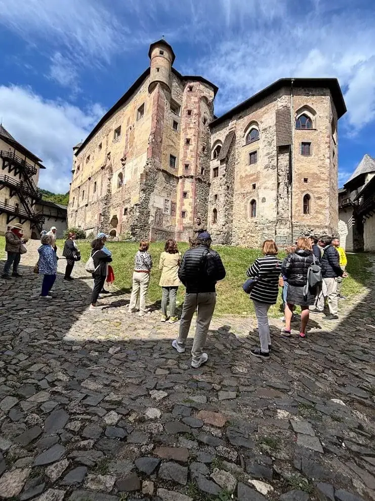 A tour group with their guide in the cobbled courtyard of a stone castle, its painted Renaissance façade above them.