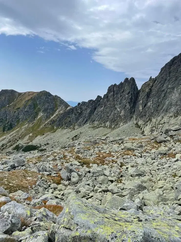 A boulder field of pale granite below the rock spires of a Tatra ridge, lichen and autumn grass between the stones.