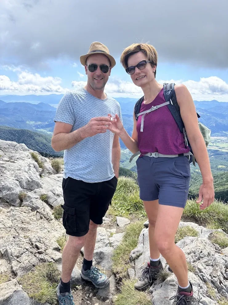 Two walkers sharing a small glass on a rocky summit in the Malá Fatra, the valley far below.