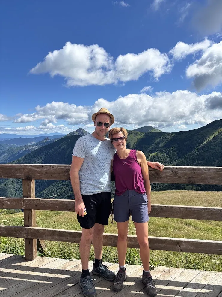 Two walkers at a wooden viewpoint rail in the Malá Fatra, green ridges and summer cloud behind them.