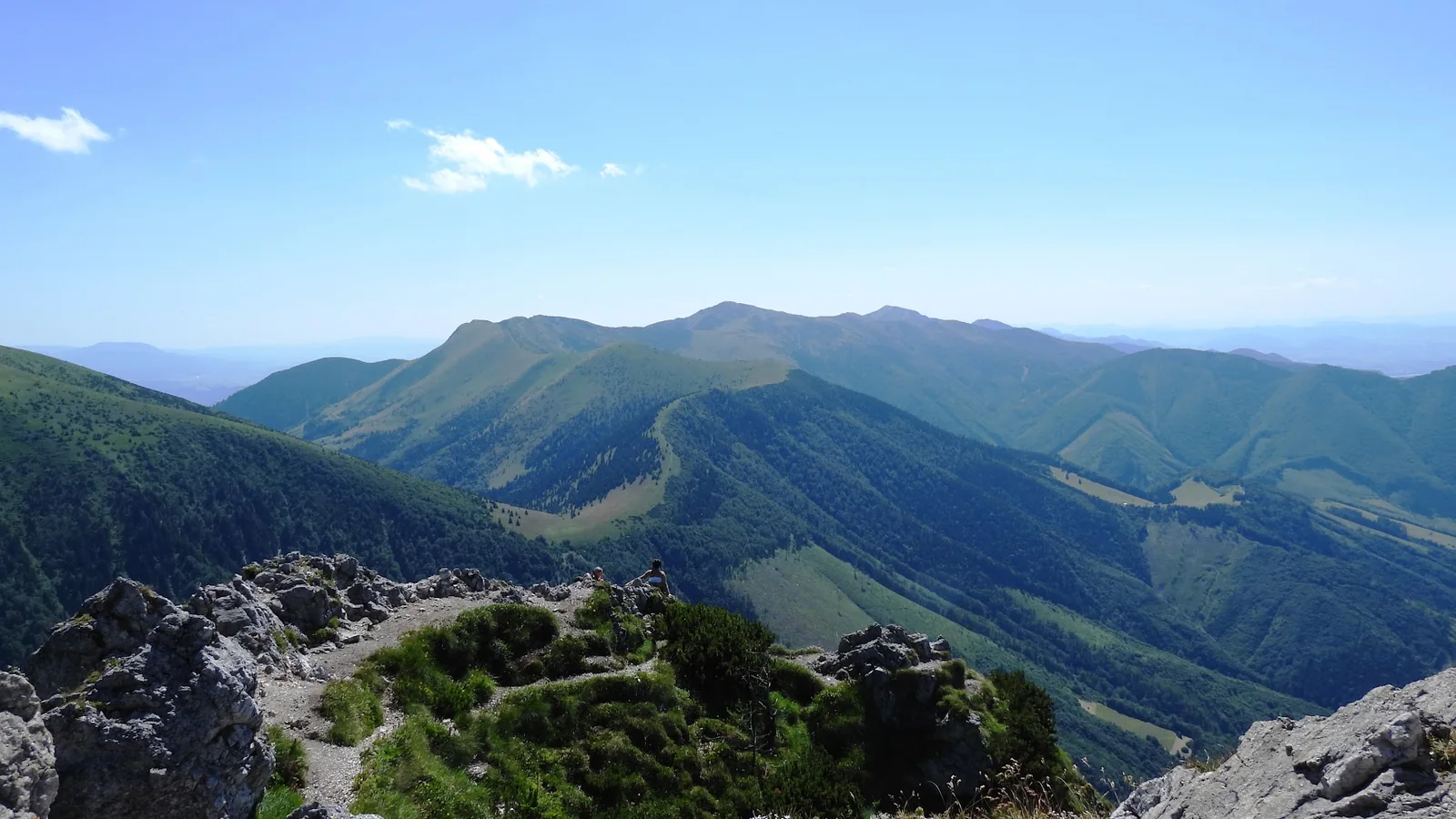 The long green ridges of the Malá Fatra seen from a rocky summit, walkers resting on the rocks and valleys falling away on both sides.