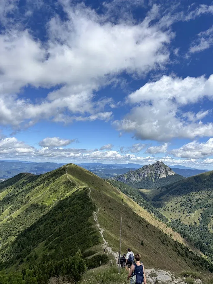 Walkers descending a narrow ridge path in the Malá Fatra, the rocky peak of Rozsutec beyond the valley.