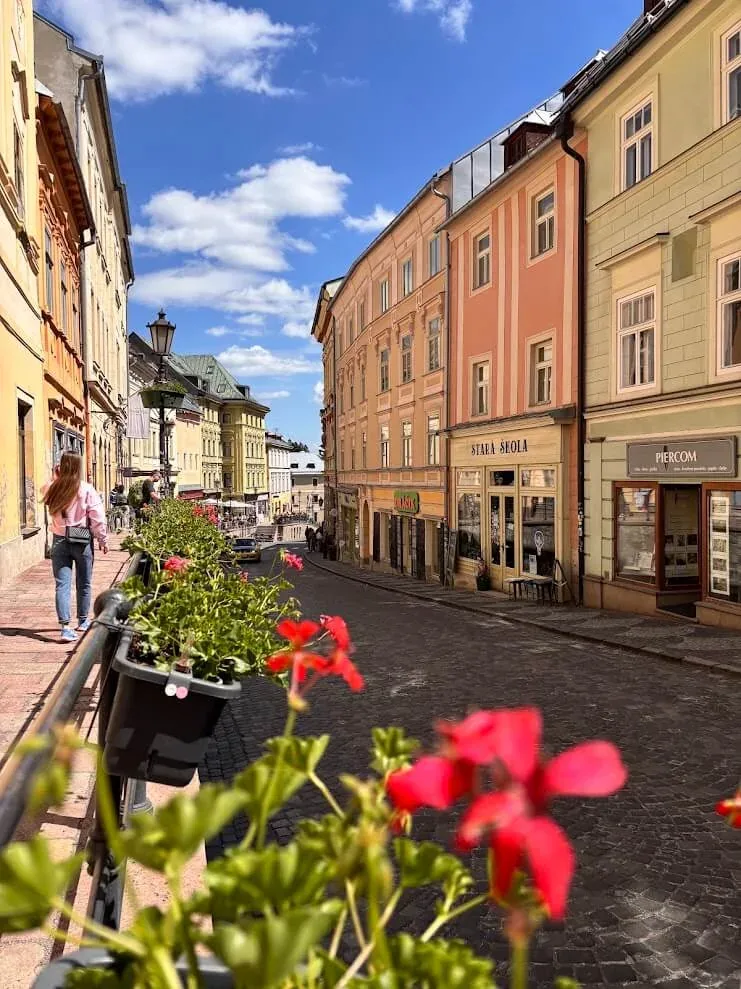 A cobbled street of pastel houses in a Slovak mining town, red geraniums on the railing in the foreground.