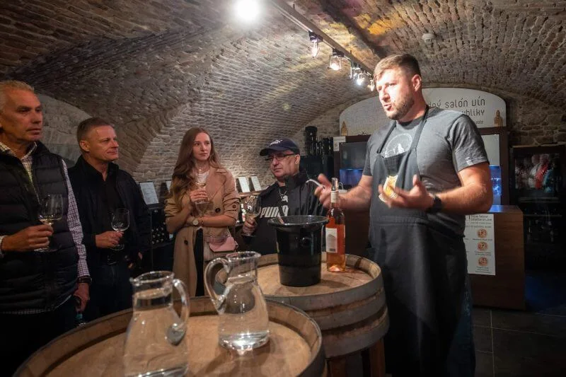 A sommelier presenting a bottle to a small group at a wine tasting in the brick-vaulted cellar of the National Salon of Wines in Bratislava.