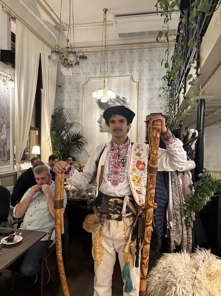 A musician in embroidered Slovak folk costume holding two carved fujara shepherd’s flutes at a folk dinner in Café Štefánka, Bratislava.
