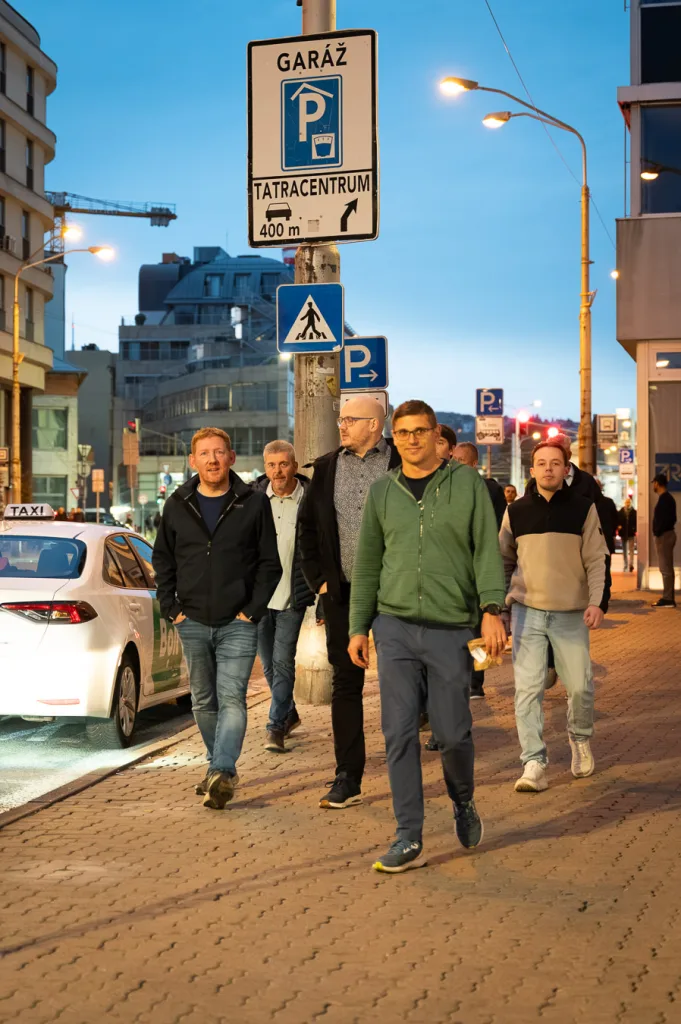 A corporate group walking through the centre of Bratislava at dusk with their guide, passing the signpost for the Tatracentrum car park.