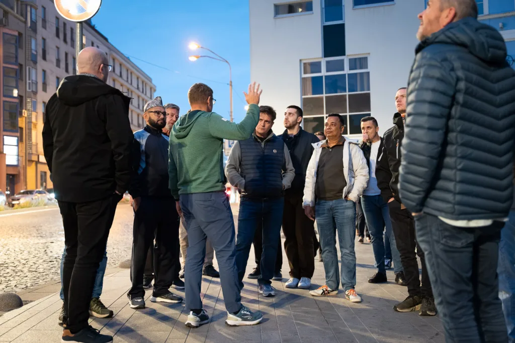 A guide briefing a corporate group on a Bratislava street at dusk, the delegates gathered in a half circle around him.