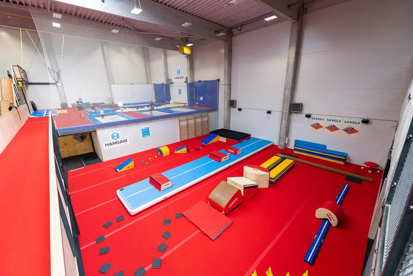 The HangAir trampoline and gymnastics hall in Bratislava laid out for a team activity, with an airtrack, vaulting blocks, a beam and foam obstacles set out on red carpet.