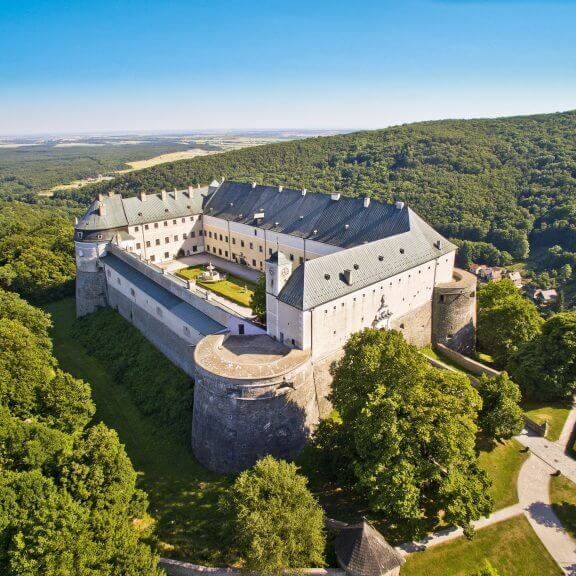 Majestic view of a historic Red Stone Castle surrounded by lush green forests, a perfect stop on an Incentive Nature Bratislava Getaway.