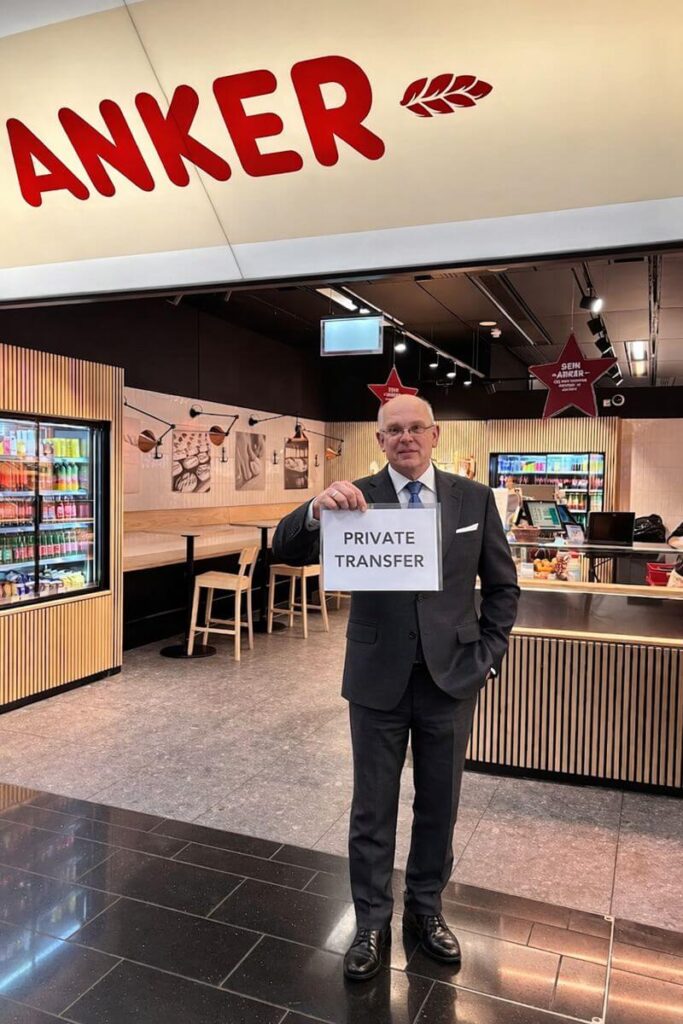 Conductor profesional de traslado privado sosteniendo un cartel que dice “Private Transfer” en el área de llegadas del aeropuerto de Viena.