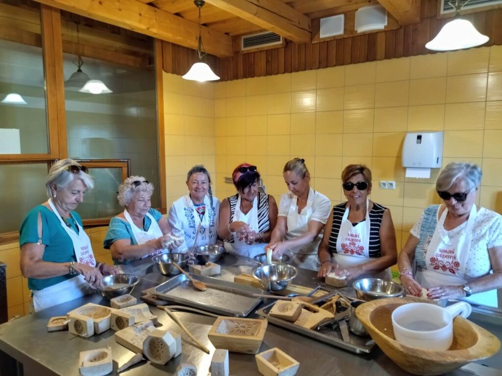 Un groupe de femmes participe à un atelier culinaire traditionnel slovaque, préparant des biscuits ou du pain dans une ambiance chaleureuse et conviviale.